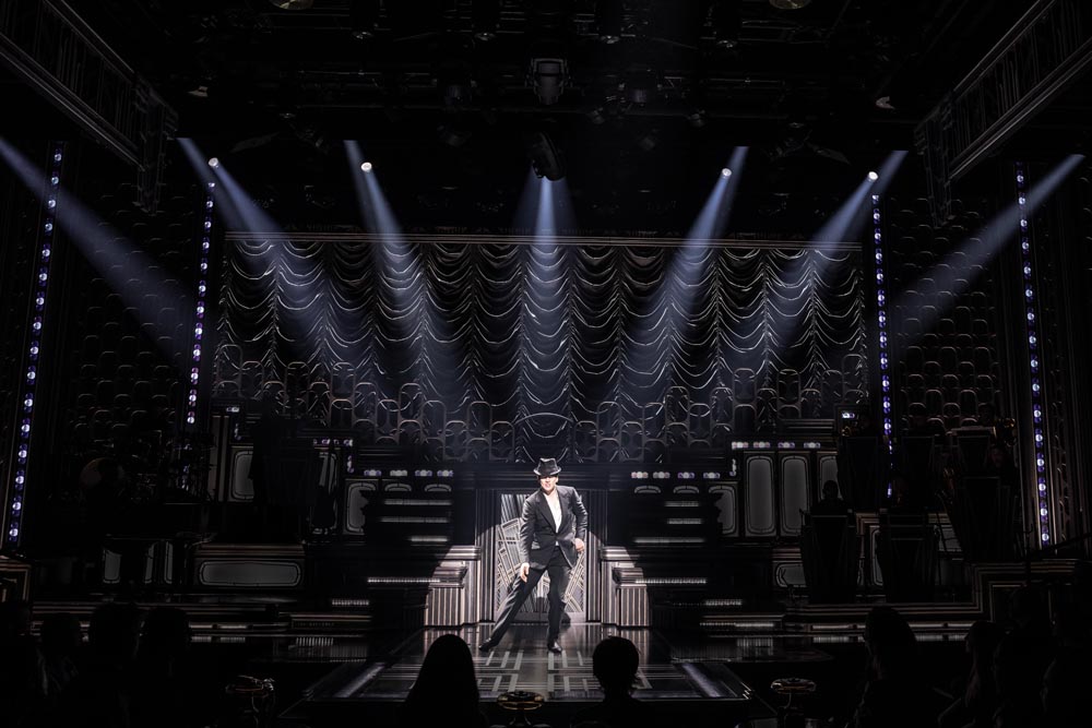 Jonathan Groff as Bobby Darin performs on stage, illuminated by dramatic lighting against a textured backdrop.
