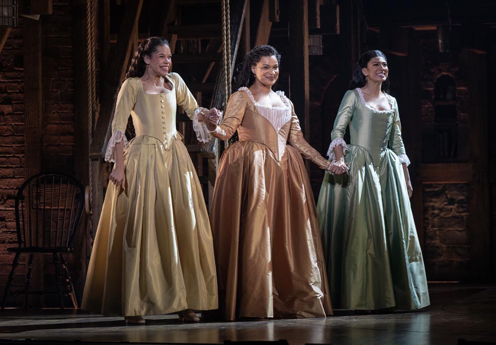 Lily Soto, Marja Harmon, and Lauren Mariasoosay in elegant gowns, performing together on stage in Hamilton.