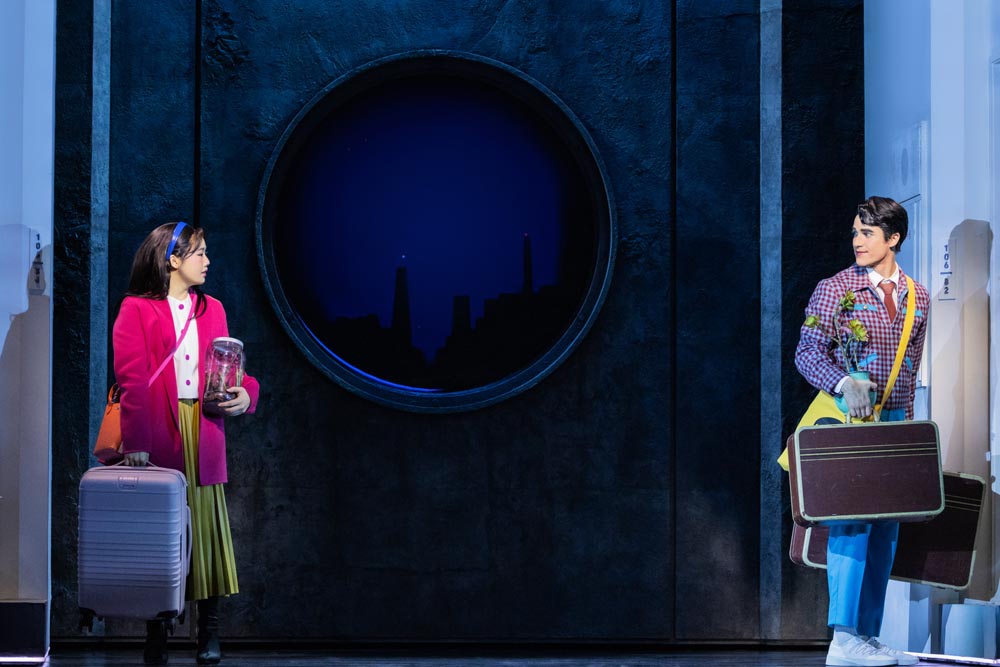 Helen J. Shen and Darren Criss stand on stage, each holding props, against a dark backdrop.