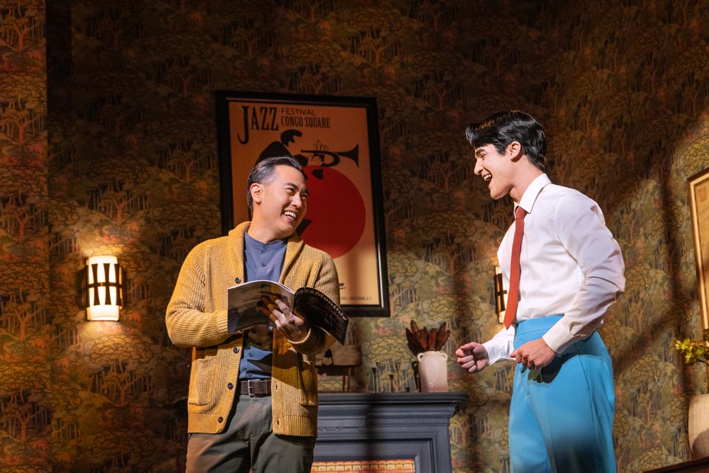 Marcus Choi and Darren Criss perform on stage, smiling, with a vintage jazz-themed backdrop and warm lighting.